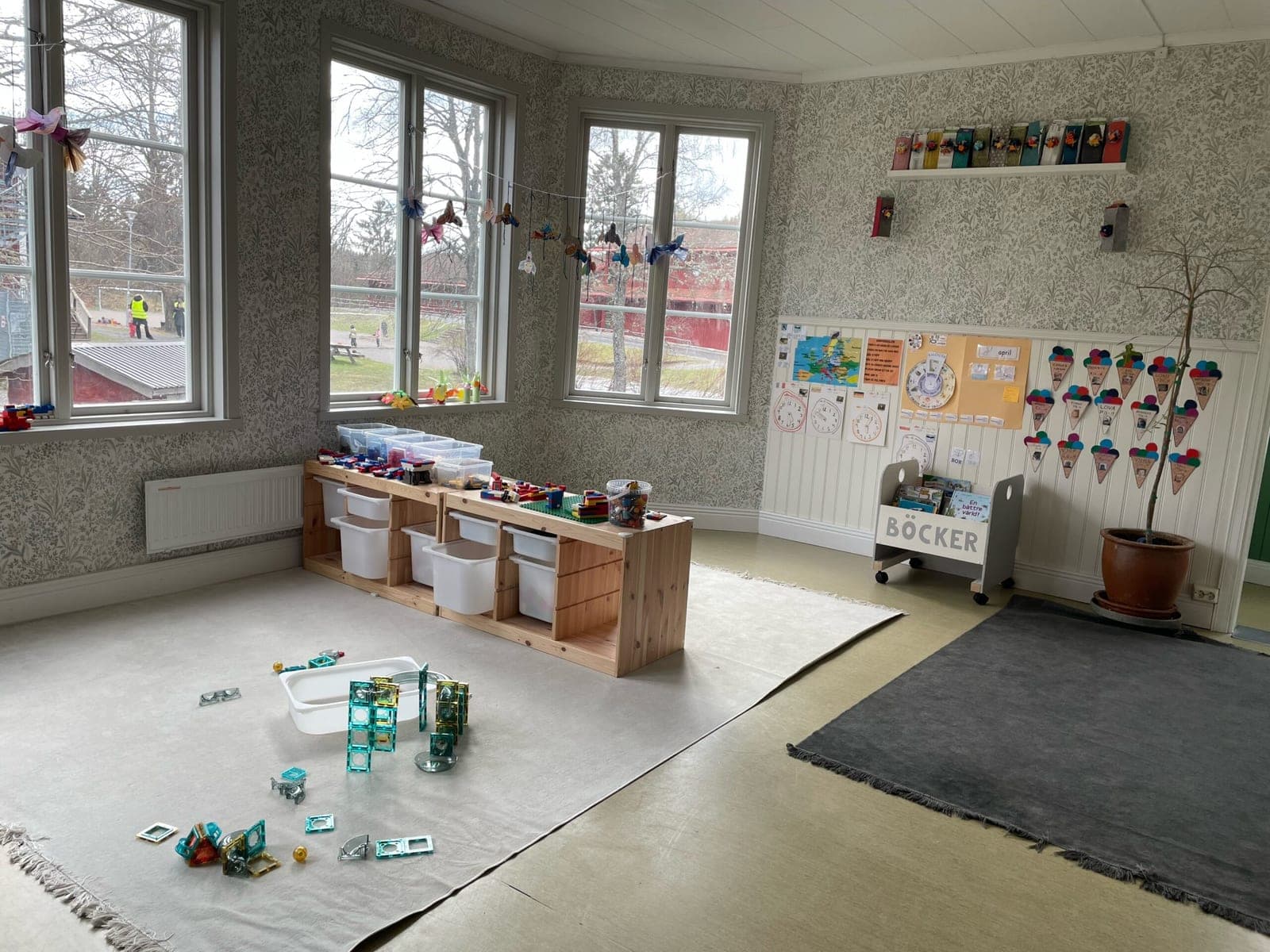 Solrosens ljusa rum i Riala gamla kyrkskola med byggmaterial, bokhylla och blommönstrad tapet.